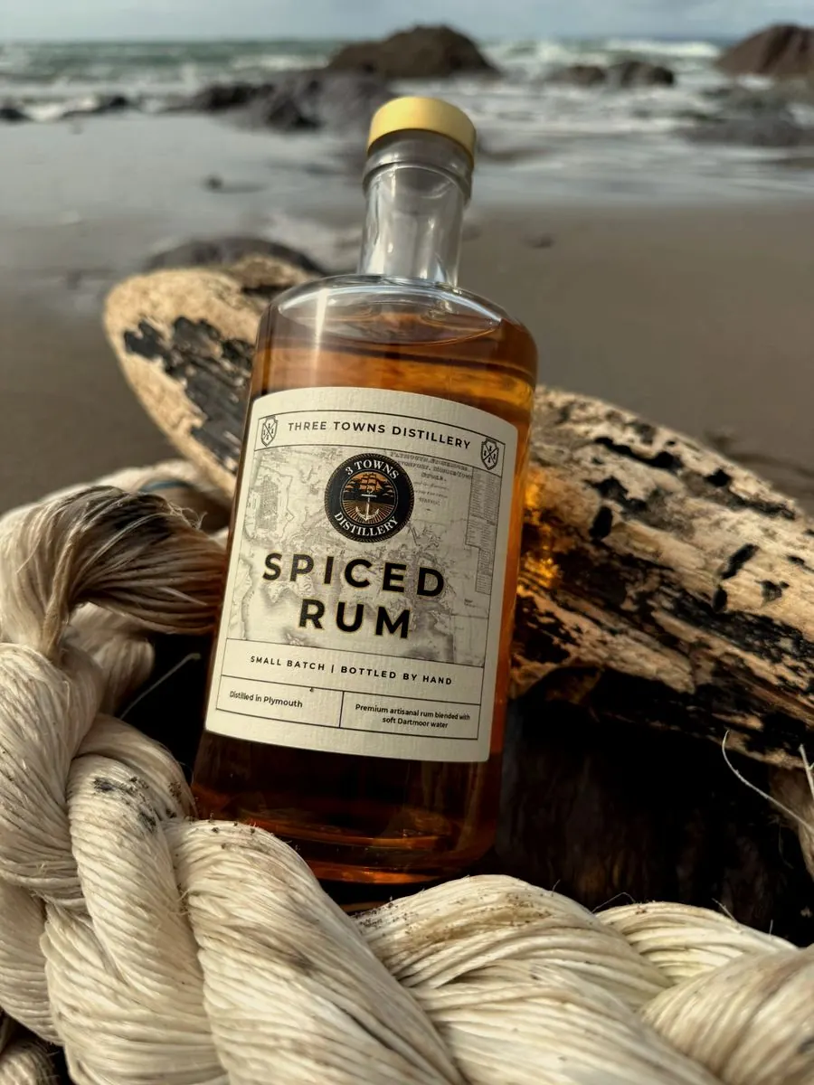 Three Towns Spiced Rum bottle nestled in rope on a Plymouth beach