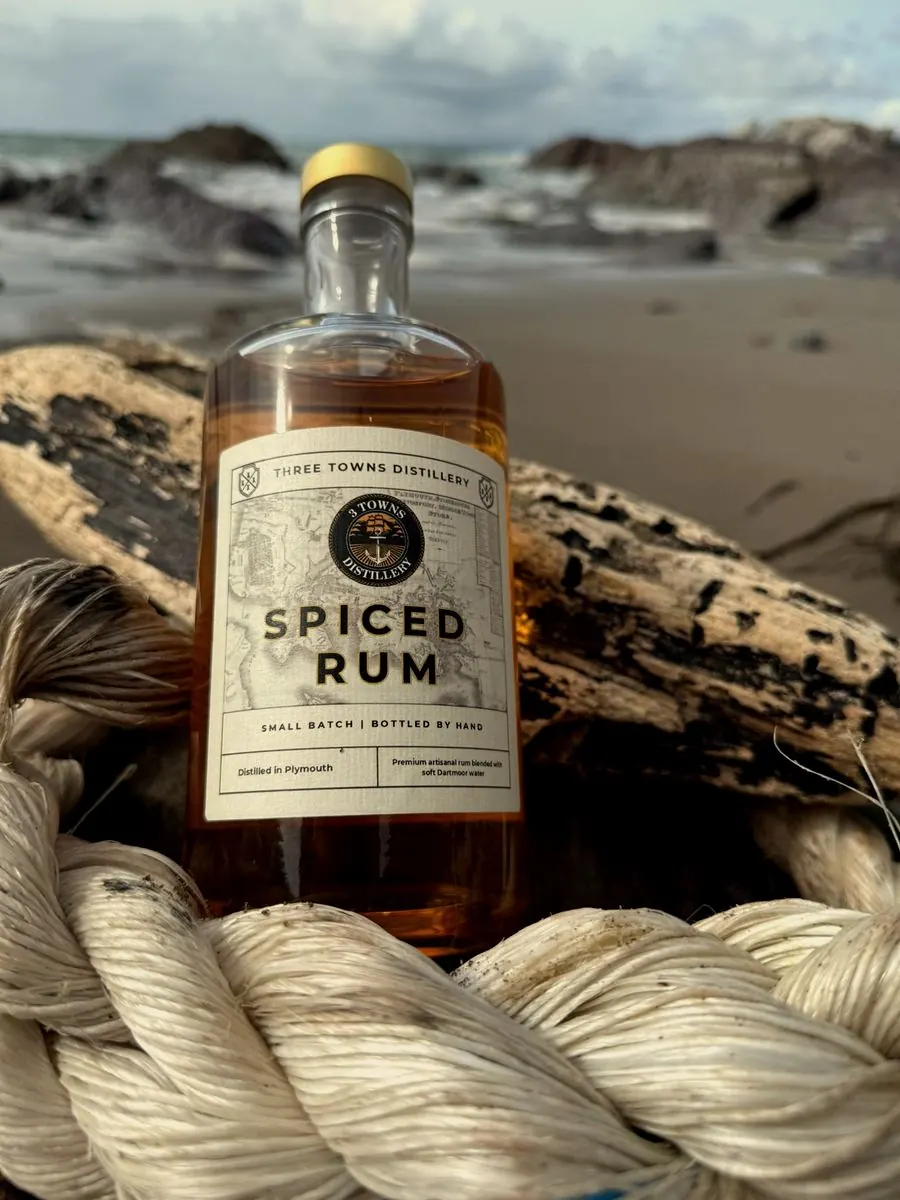 Three Towns Spiced Rum bottle on driftwood at the Plymouth coastline