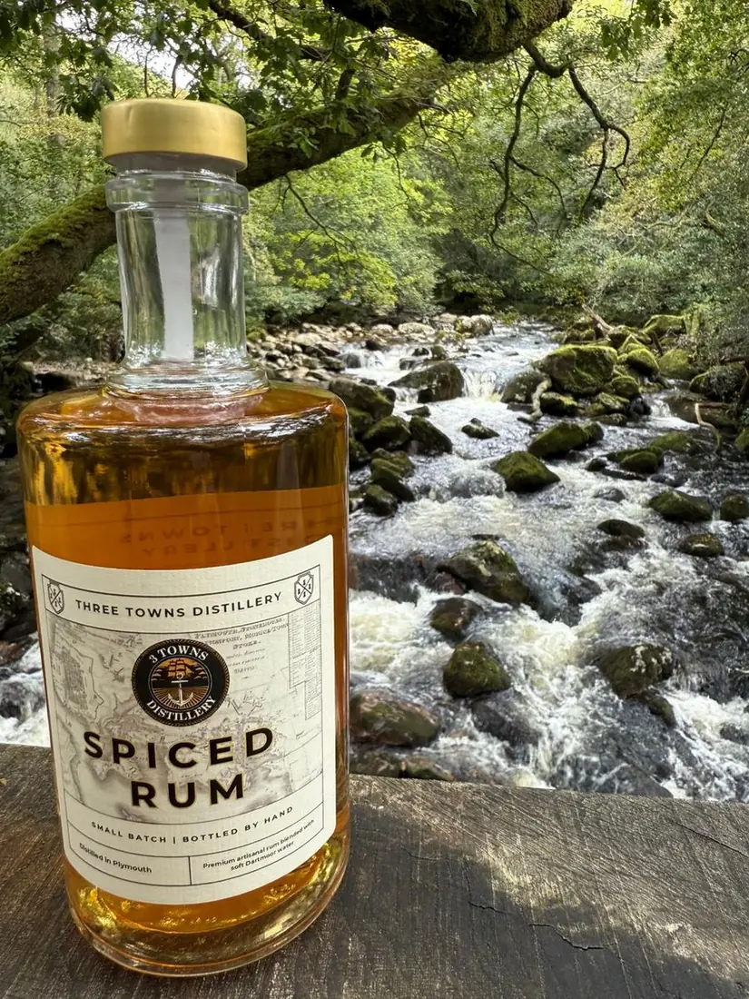 Three Towns Spiced Rum bottle resting on rocks in a Dartmoor river